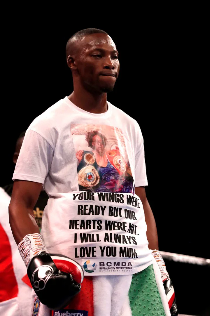 Un boxeador con guantes viste una remera blanca con una foto y un mensaje impreso dedicado a su madre.