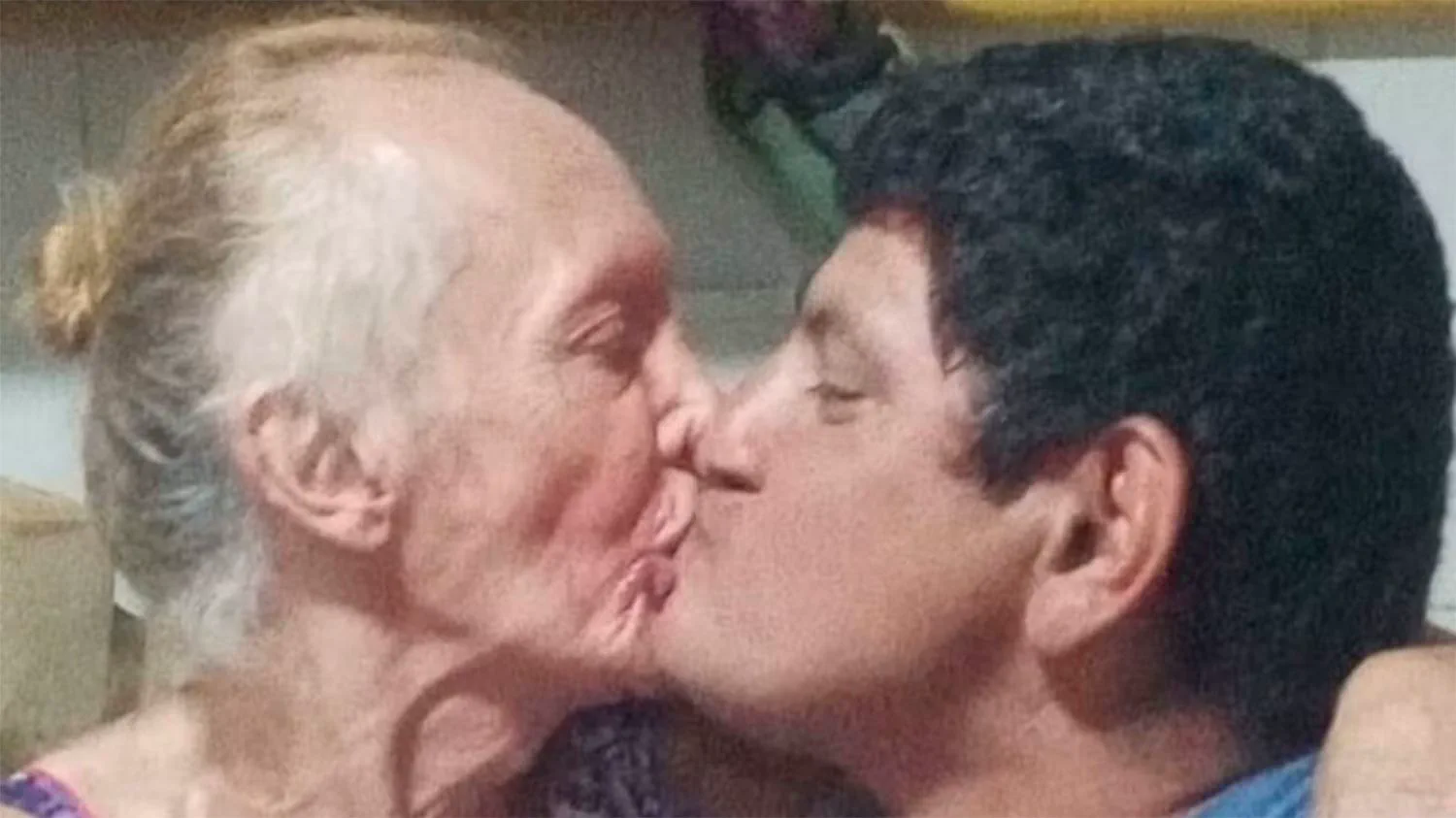Primer plano de una mujer mayor y un hombre besándose en la boca.